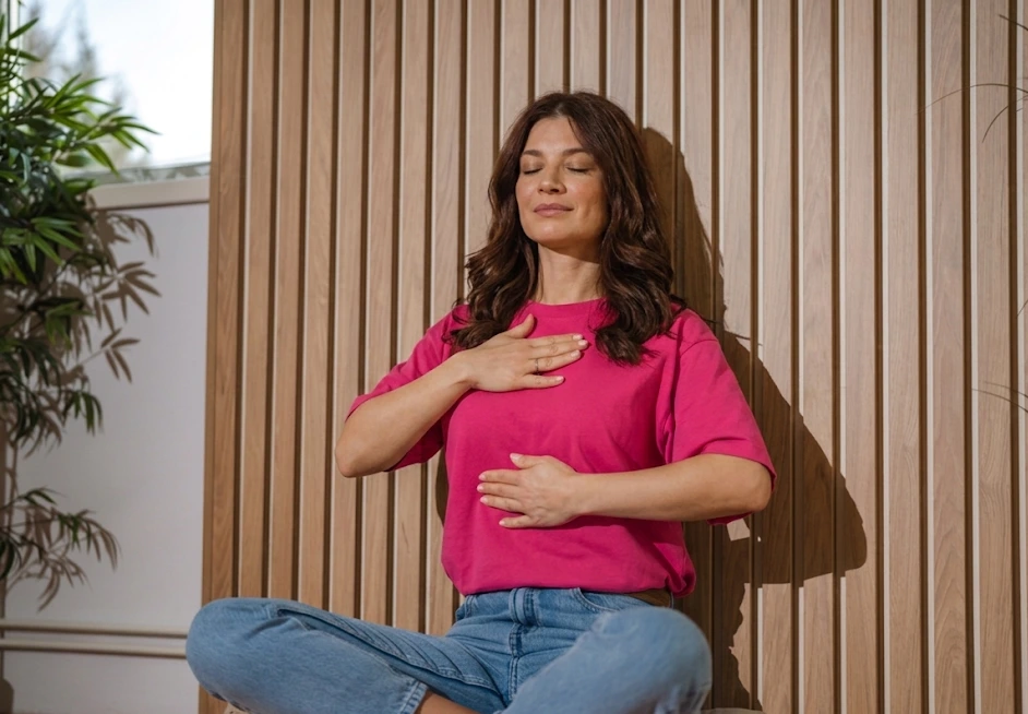 Femme enceinte assise paisiblement près d'une fenêtre, une main sur le ventre, concentrée sur sa respiration dans une lumière douce